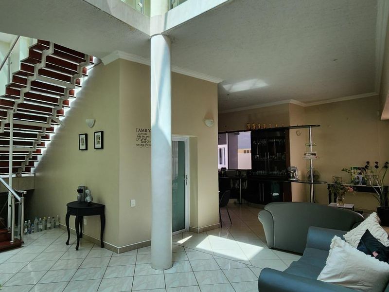 Spacious open-plan living area featuring a prominent staircase with stainless steel balustrades, tiled flooring, and a built-in bar area.