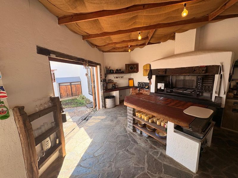 Covered outdoor entertainment area featuring a built-in braai, stone flooring, and rustic exposed timber ceiling, providing a functional space for alfresco dining.