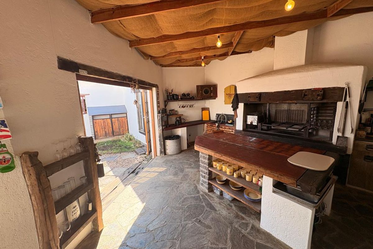 Covered outdoor entertainment area featuring a built-in braai, stone flooring, and rustic exposed timber ceiling, providing a functional space for alfresco dining.