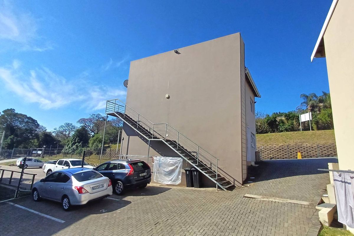 Exterior view of an apartment building featuring an external metal staircase and paved parking area.