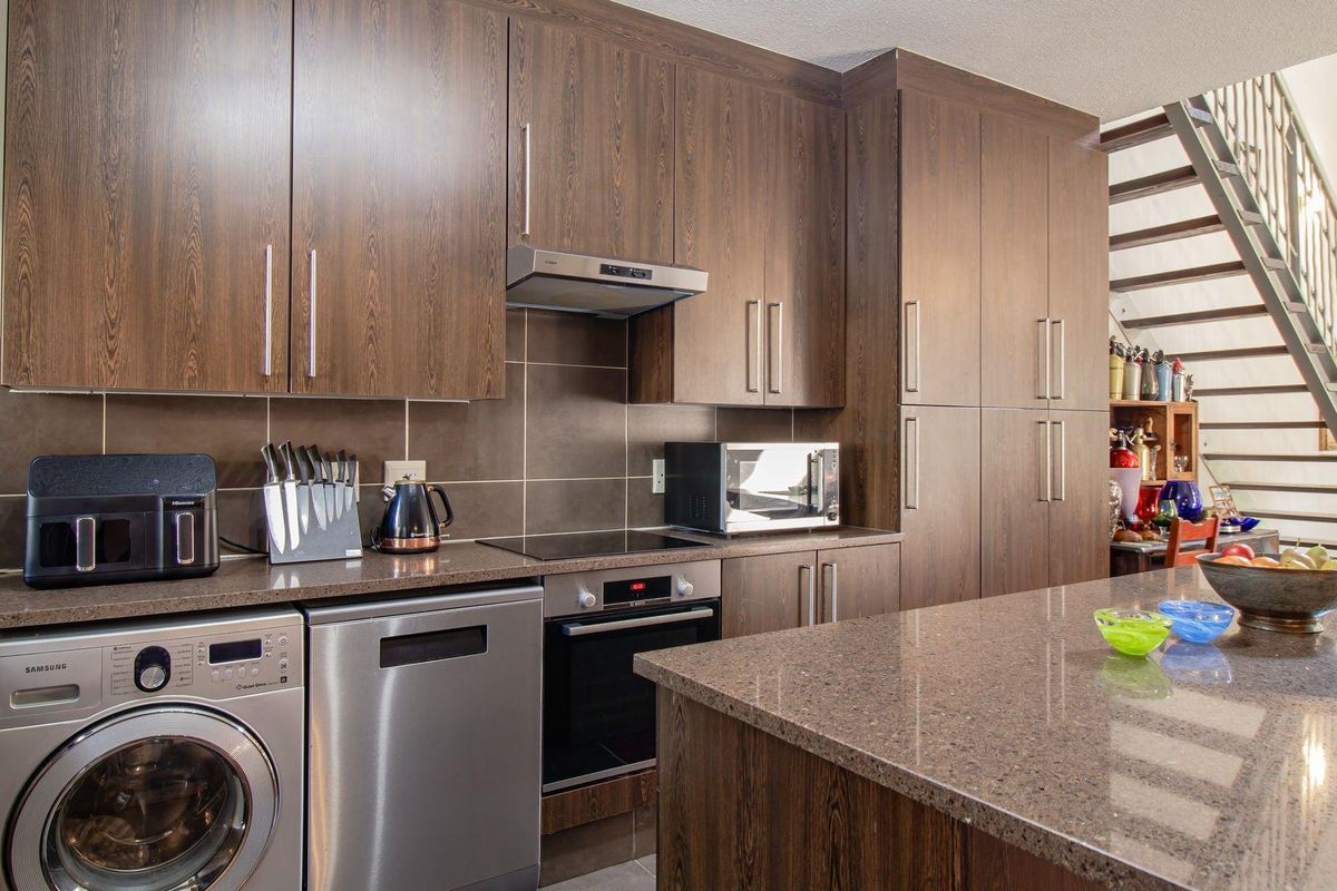 Modern kitchen featuring dark wood cabinetry, stone countertops, integrated oven, hob, extractor fan, and a dedicated space for laundry appliances.