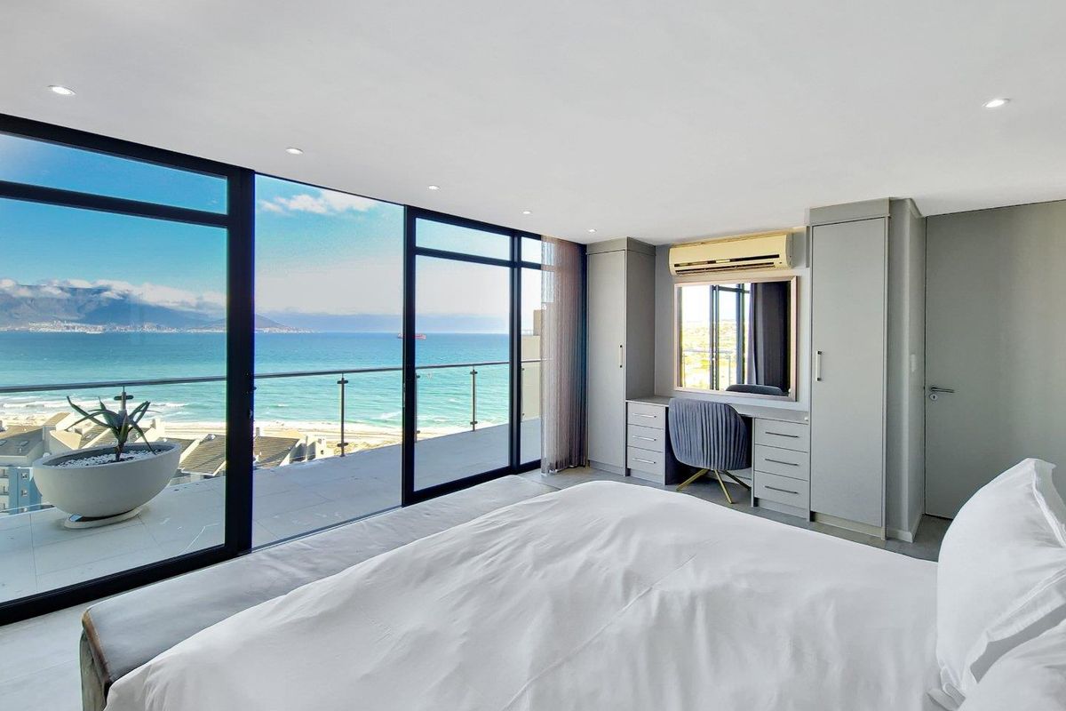 Spacious bedroom featuring floor-to-ceiling glass sliding doors, built-in cabinetry with integrated vanity, and direct access to a private balcony with panoramic ocean views.