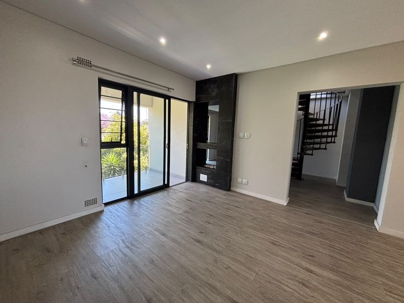 Spacious living area featuring modern laminate flooring, a built-in fireplace, recessed lighting, and sliding glass doors leading to an outdoor balcony.