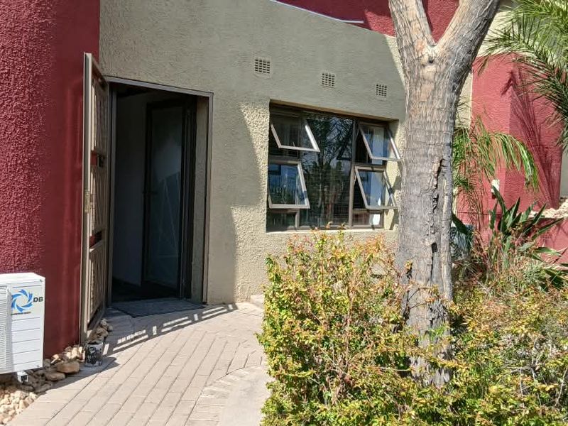 Front entrance of the office building featuring a paved walkway, security door, and exterior air conditioning unit.