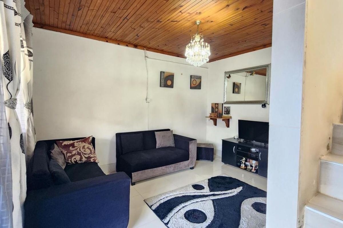 Living room featuring a timber-clad ceiling, tiled flooring, and an adjacent staircase, offering a functional space with potential for modern updates.