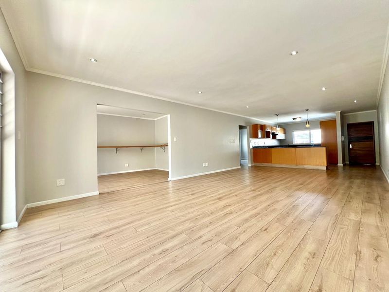 Spacious open-plan living area featuring modern laminate flooring, recessed lighting, and a functional kitchen with built-in cabinetry and a central island.