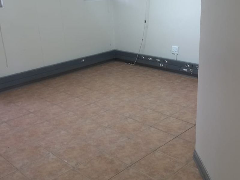 A clean, empty office space featuring tiled flooring, integrated electrical trunking for workstations, and neutral wall finishes.