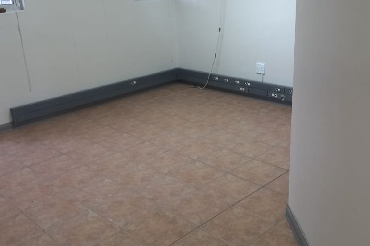 A clean, empty office space featuring tiled flooring, integrated electrical trunking for workstations, and neutral wall finishes.