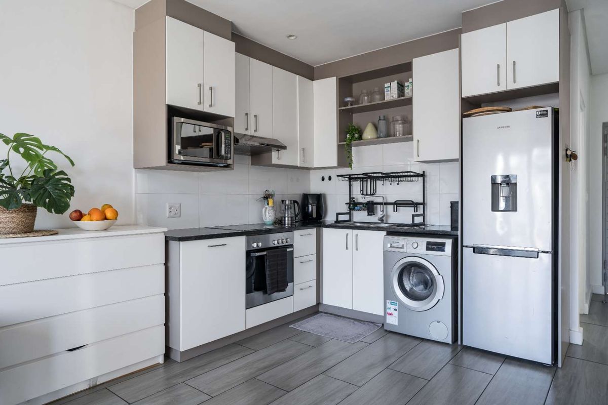 Modern kitchen featuring white cabinetry, dark stone countertops, built-in oven, hob, extractor fan, and integrated space for a washing machine.