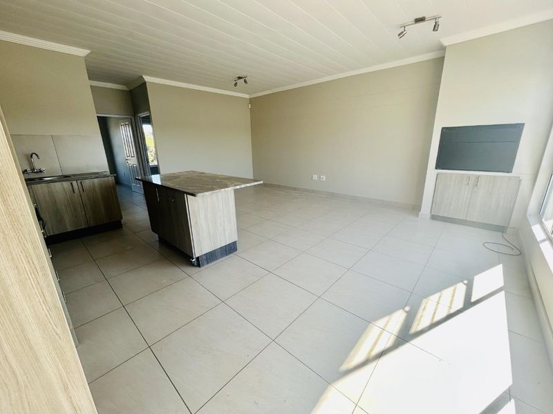 Spacious open-plan living area featuring a modern kitchen with a central island, stone countertops, and neutral tiled flooring throughout.