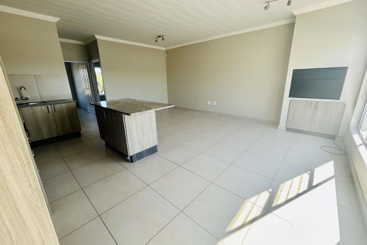 Spacious open-plan living area featuring a modern kitchen with a central island, stone countertops, and neutral tiled flooring throughout.