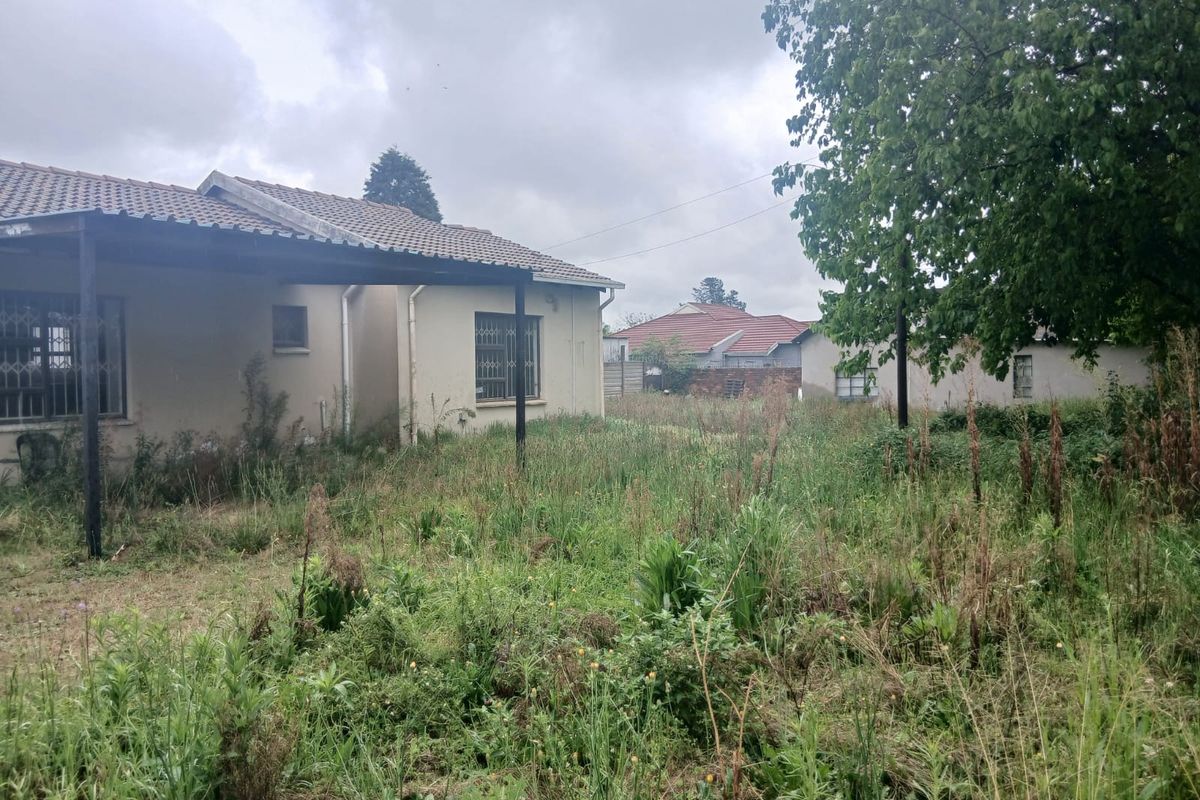 Rear view of the property featuring a covered patio and an expansive, overgrown garden area with established trees and boundary walling.