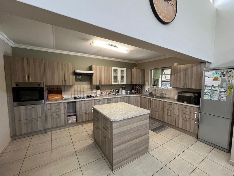 Spacious kitchen featuring wood-look cabinetry, a central island, built-in oven, gas hob, and tiled flooring with ample storage and workspace.