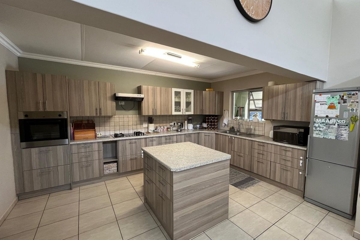 Spacious kitchen featuring wood-look cabinetry, a central island, built-in oven, gas hob, and tiled flooring with ample storage and workspace.