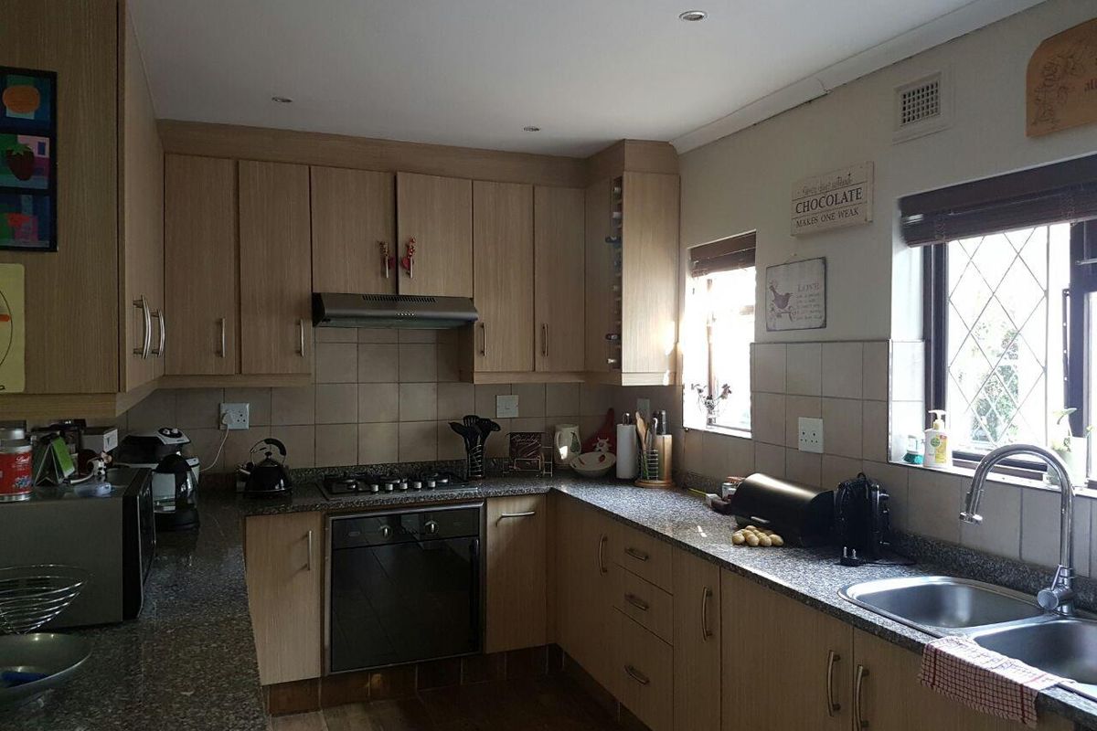 A functional kitchen featuring light wood cabinetry, granite countertops, a gas hob, built-in oven, and a double basin sink with tiled backsplash.