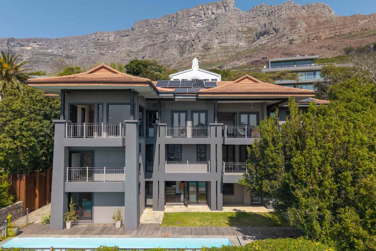 Rear elevation of a multi-story residence featuring multiple balconies, a swimming pool, timber decking, and solar panels set against a mountain backdrop.