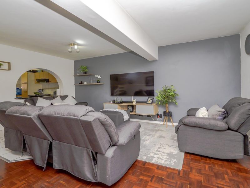 Open plan living area featuring parquet flooring, a structural ceiling beam, and an arched opening leading to the kitchen space.