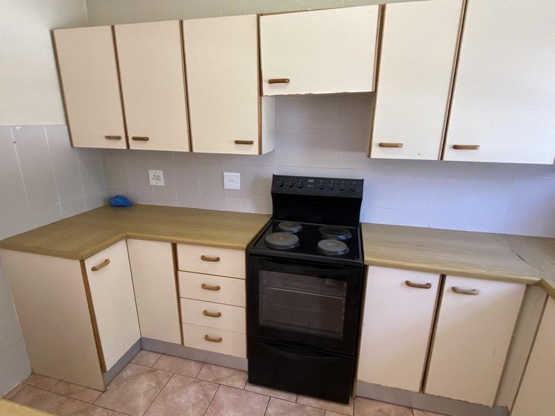 A functional kitchen featuring laminate countertops, tiled backsplash, built-in cabinetry, and a freestanding electric stove with oven.