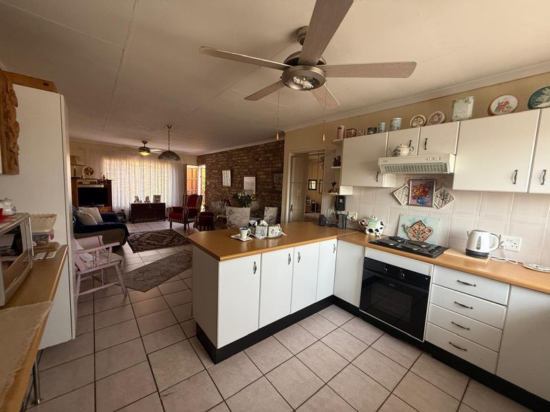 Open-plan living area featuring a functional kitchen with built-in cabinetry, gas hob, and oven, flowing into a spacious lounge with exposed brick accents.