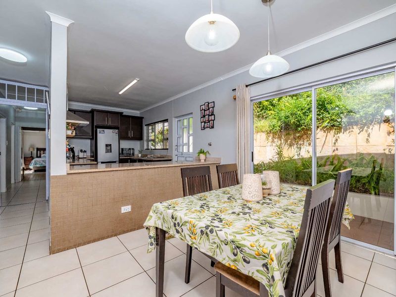 Open-plan dining and kitchen area featuring tiled floors, dark cabinetry, granite countertops, and sliding glass doors leading to the garden.