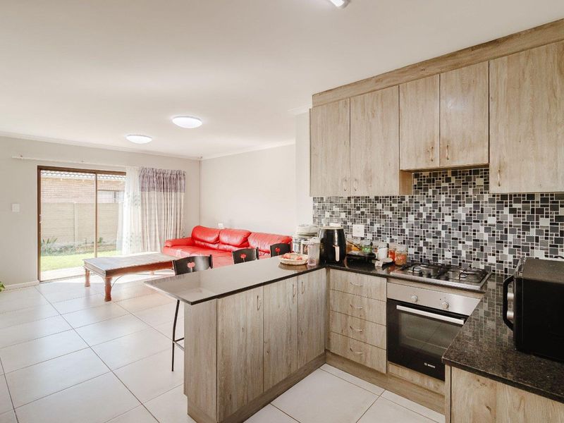 Open-plan living area featuring a modern kitchen with wood-finish cabinetry, granite countertops, mosaic backsplash, and direct access to the rear garden via sliding doors.