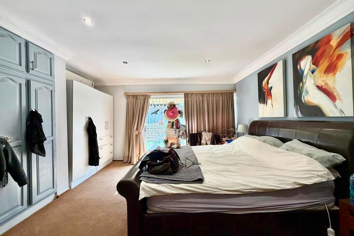 Spacious bedroom featuring built-in cupboards, recessed downlighting, decorative ceiling cornices, and direct access to an outdoor area through sliding glass doors.