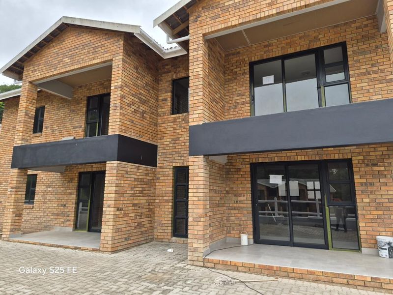 A modern double-story apartment building featuring face brick construction, dark-framed sliding glass doors, and paved ground-floor patio areas.