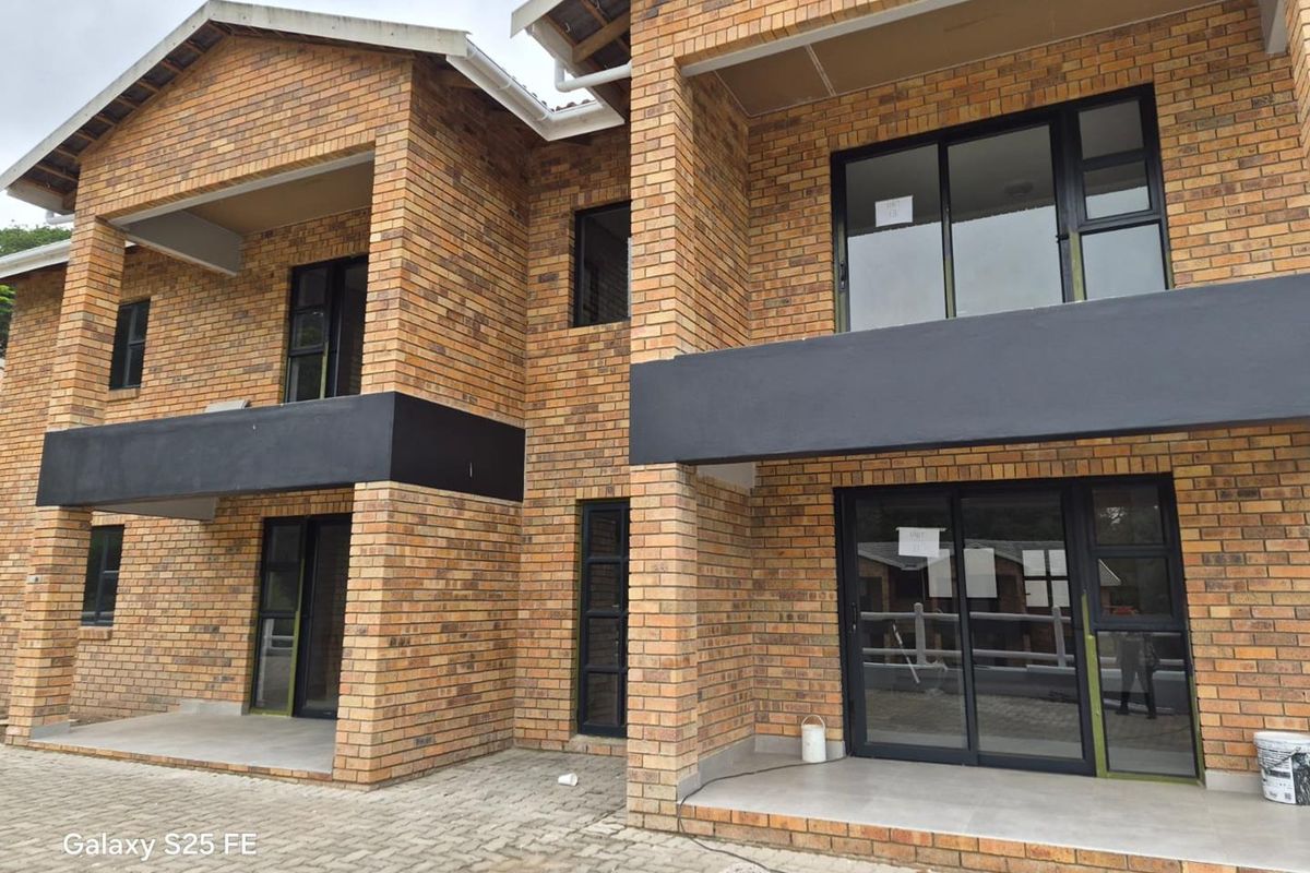 A modern double-story apartment building featuring face brick construction, dark-framed sliding glass doors, and paved ground-floor patio areas.