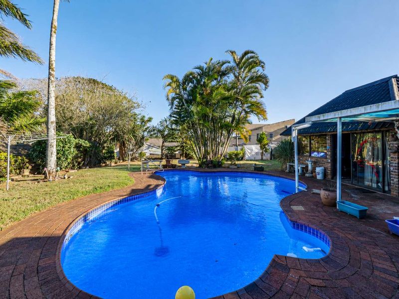 A backyard area featuring a swimming pool with brick paving and a covered patio attached to the main house structure.