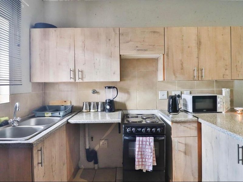 Functional kitchen featuring light wood-look cabinetry, granite-style countertops, tiled backsplash, and a built-in electric stove with double sink.