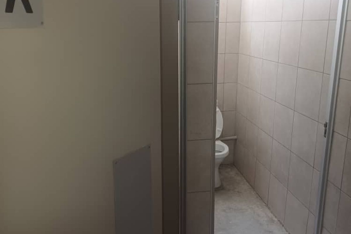 A functional restroom facility featuring tiled walls and a standard toilet fixture, currently requiring cosmetic updates to the flooring and finishes.