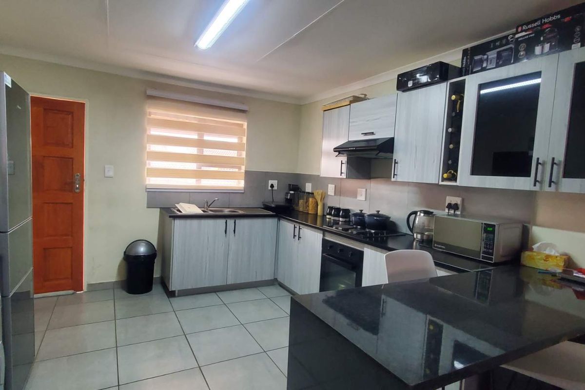 A functional kitchen featuring modern cabinetry, granite countertops, a built-in oven and hob, and tiled flooring with an integrated breakfast nook.
