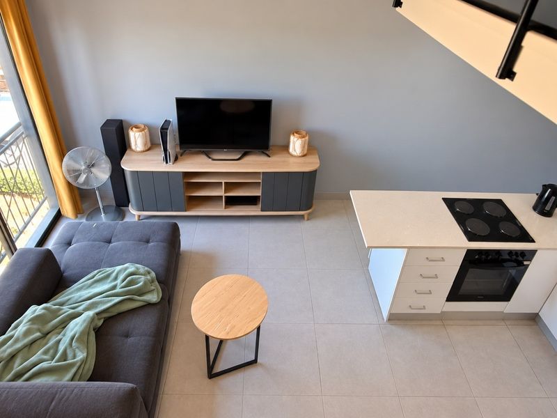 Modern open-plan living area featuring a compact kitchen with built-in appliances, tiled flooring, and direct access to a private balcony.