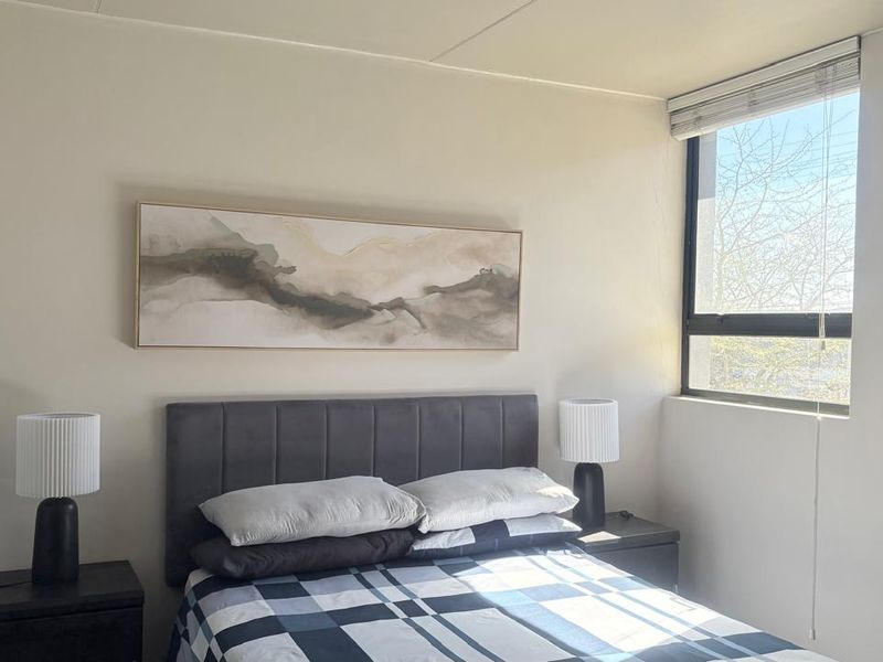A well-lit bedroom featuring neutral walls and a large window with a fitted venetian blind.