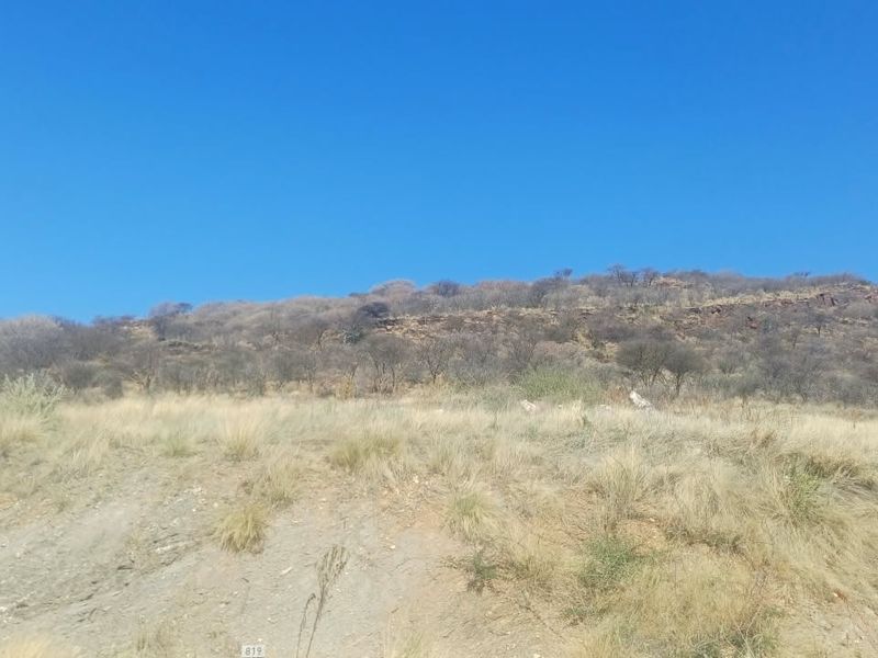 A scenic view of a natural rocky hillside with native vegetation and dry grass, showcasing the undeveloped landscape of the residential land.