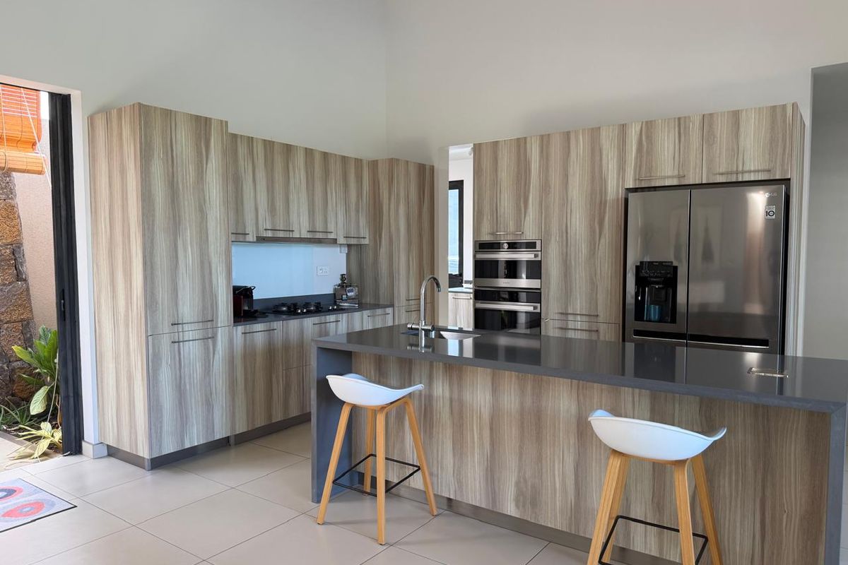 Modern kitchen featuring wood-grain cabinetry, a central island with a sink, stone countertops, and integrated stainless steel appliances.