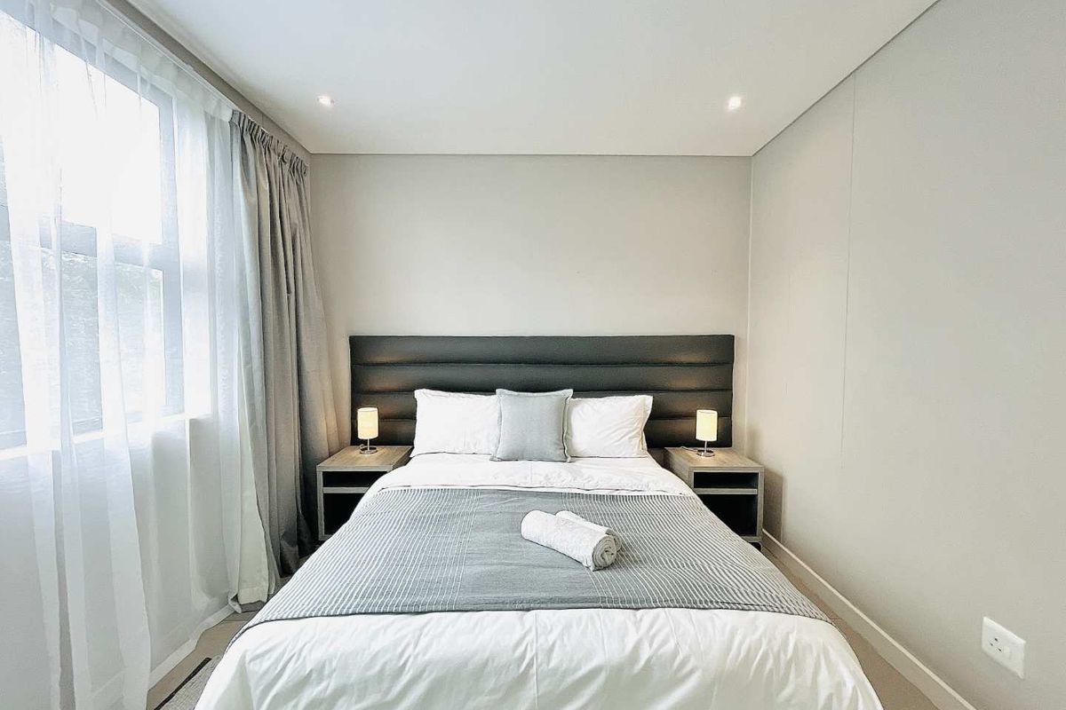 A well-maintained bedroom featuring neutral wall finishes, recessed ceiling lighting, and large windows with integrated curtain tracks.