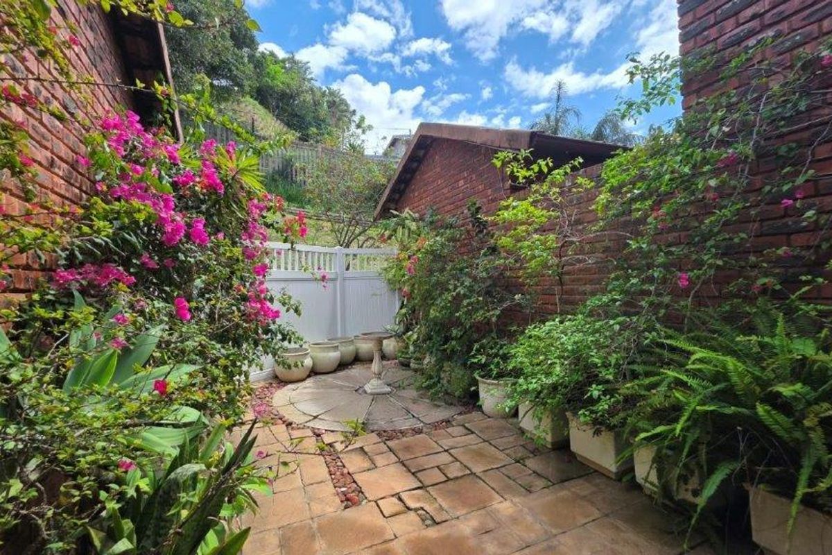 A private rear courtyard featuring brick walls, paved flooring, and established garden beds, providing a secluded outdoor space.