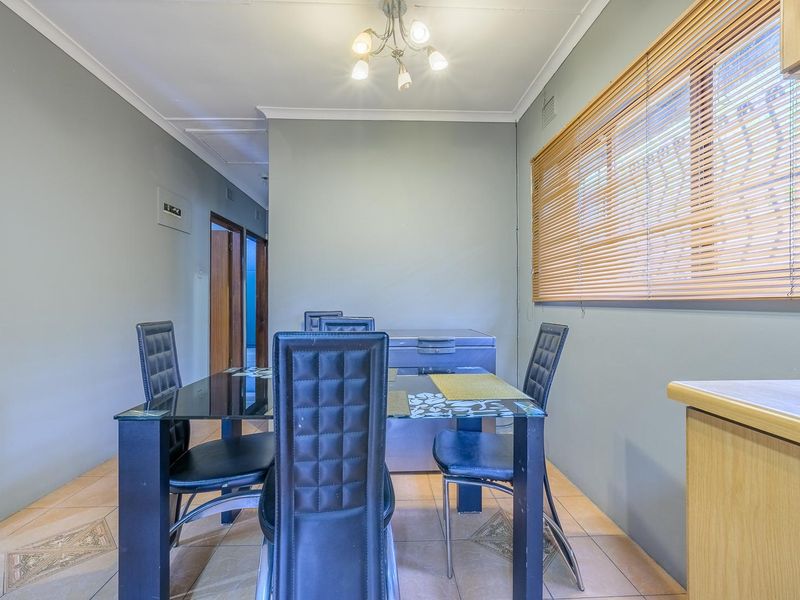 A functional dining area featuring tiled flooring, neutral wall tones, and natural light provided by a window with fitted venetian blinds.