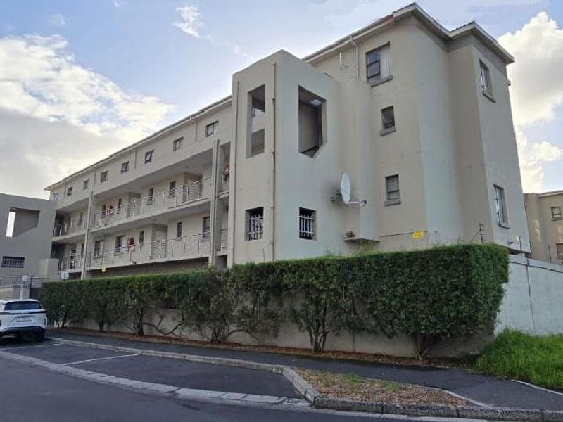 Exterior view of a multi-story apartment complex featuring balconies with metal railings and a perimeter boundary wall.