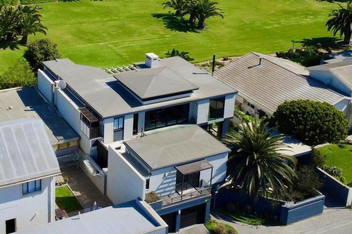 Aerial view of a modern multi-level residential property featuring flat roof architecture, balconies, and a garage, situated in a landscaped estate setting.