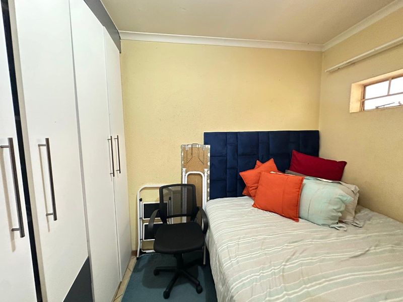 A compact bedroom featuring a built-in wardrobe, coved ceilings, and a small window, providing a functional sleeping space.