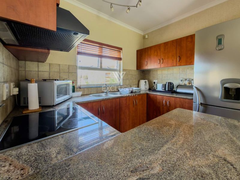 A functional kitchen featuring granite countertops, wooden cabinetry, an electric hob, and a tiled backsplash, providing a practical workspace.
