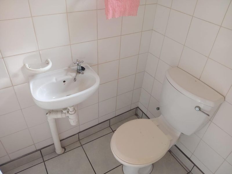 A compact bathroom featuring a wall-mounted basin and a standard toilet suite with tiled walls and flooring throughout.