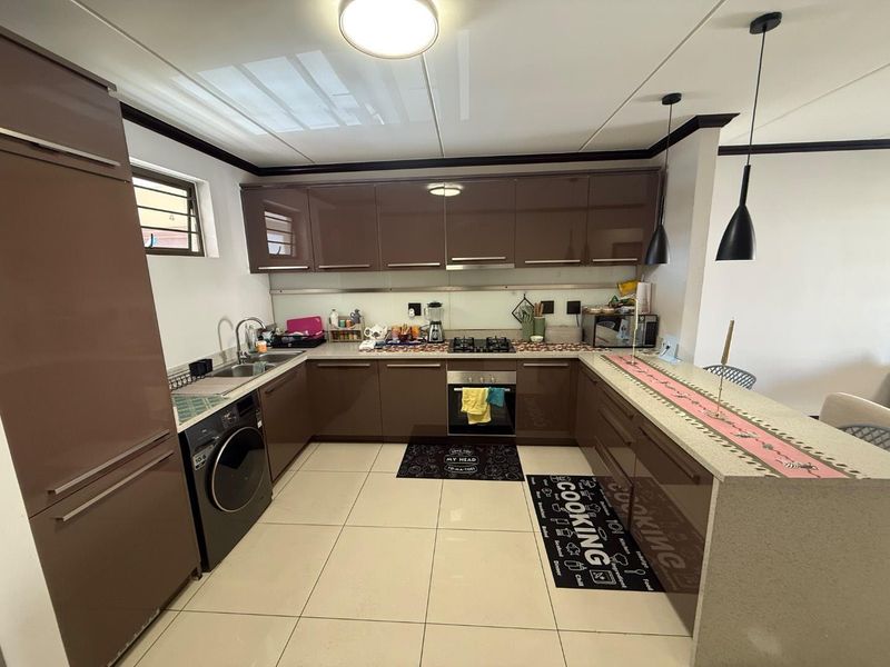 Modern kitchen featuring high-gloss cabinetry, stone countertops, integrated appliances, and a breakfast bar with pendant lighting.