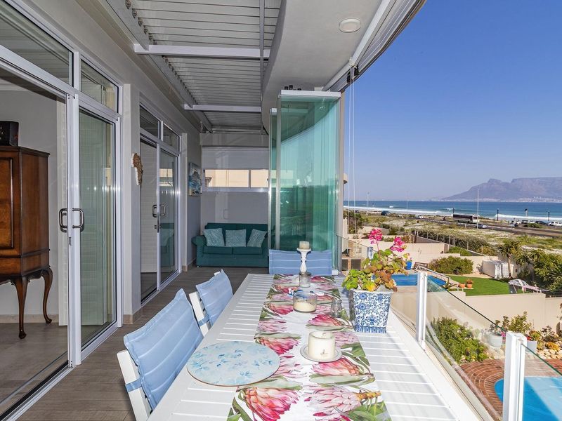 Spacious covered balcony featuring a glass balustrade, tiled flooring, and sliding door access, offering panoramic coastal and mountain views.
