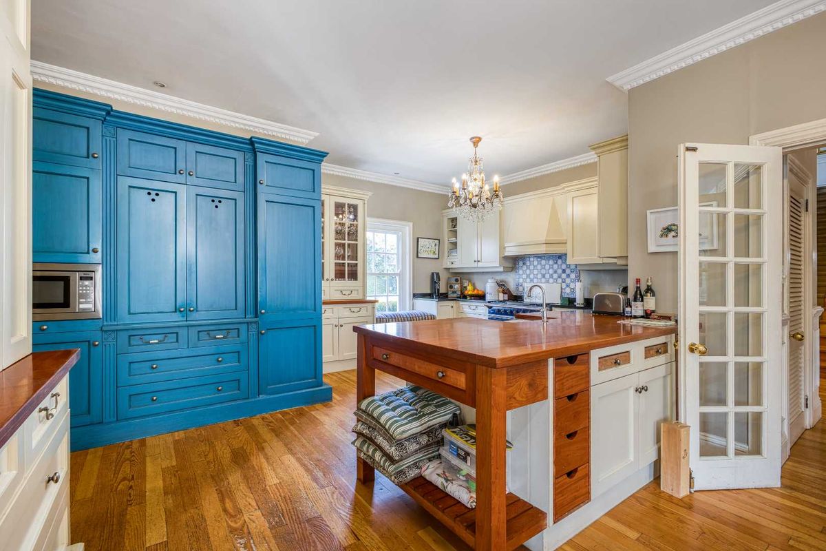 A spacious kitchen featuring a large blue cabinetry unit, a central wooden island with integrated storage, and classic crown molding throughout.