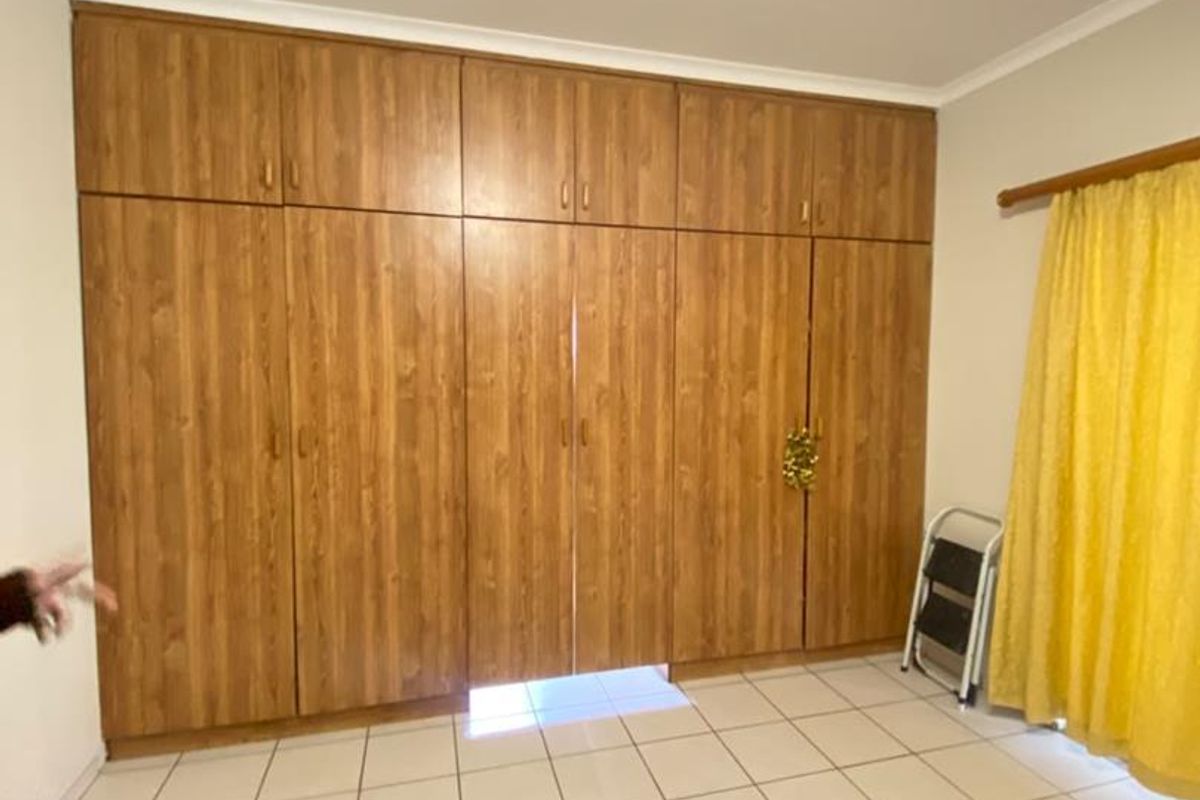 A bedroom featuring extensive floor-to-ceiling built-in wooden cupboards and neutral tiled flooring, offering ample storage space.