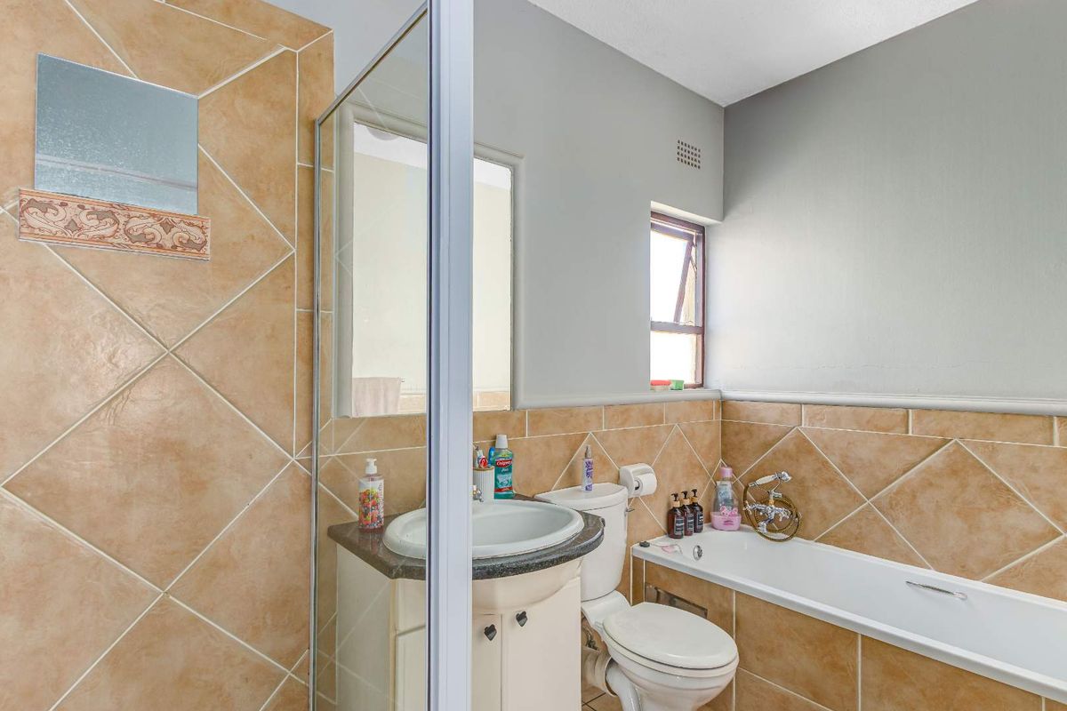 A functional bathroom featuring a built-in bathtub, a vanity with a basin, and neutral wall tiling with a decorative border.