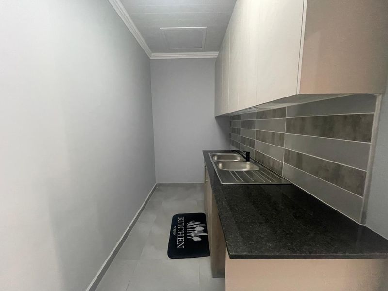 A clean and functional scullery featuring modern cabinetry, a granite countertop, and a stainless steel double sink with a tiled backsplash.